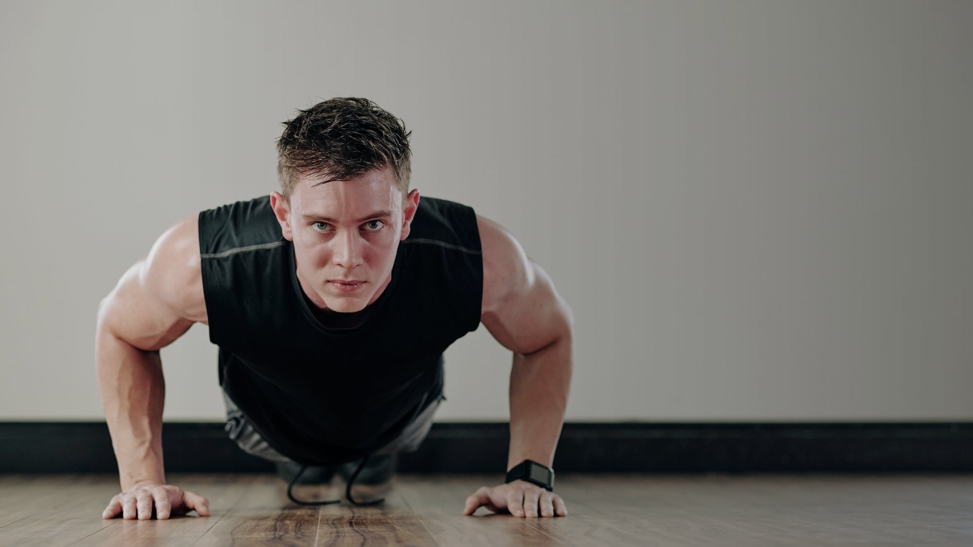Man performing push-ups on a wooden floor with a neutral background