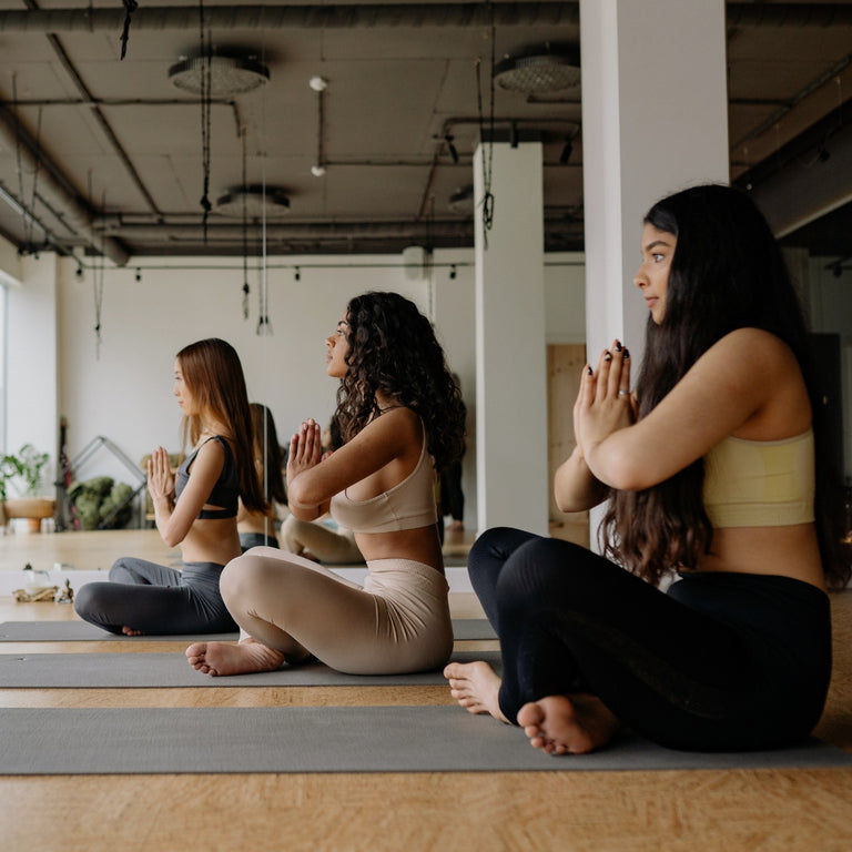 Three women practicing yoga in a studio with large windows and plants.