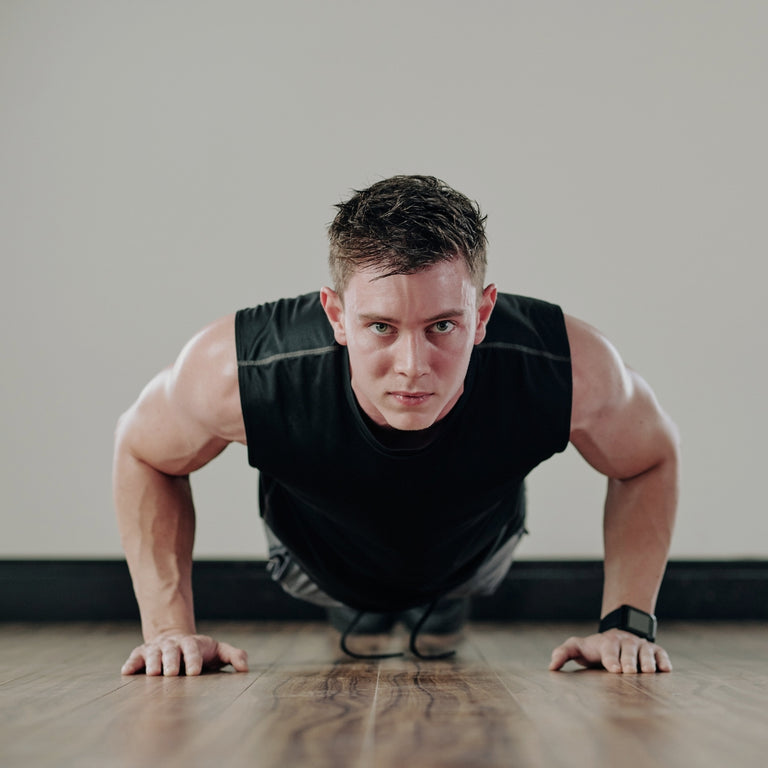 Man performing push-ups on a wooden floor with a neutral background