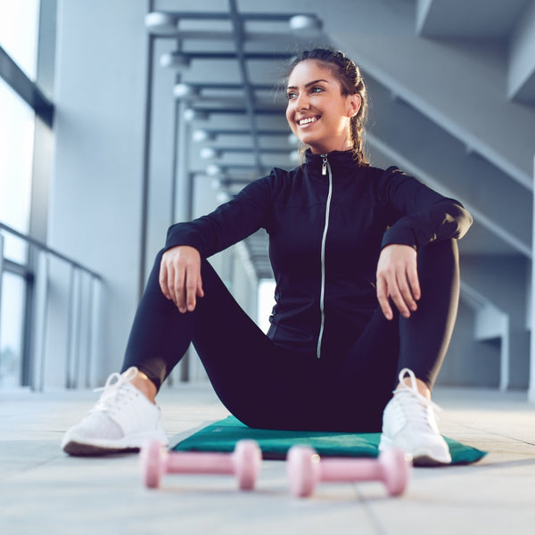 Woman in black athletic wear sitting on a mat with pink dumbbells in a modern indoor setting