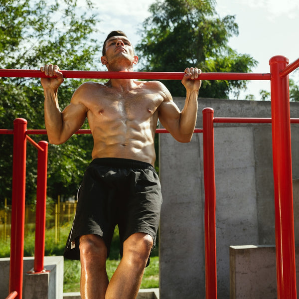 Man performing pull-ups on a red metal bar outdoors with greenery in the background
