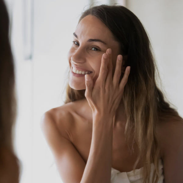 Woman with long hair smiling and touching her face against a blurred background