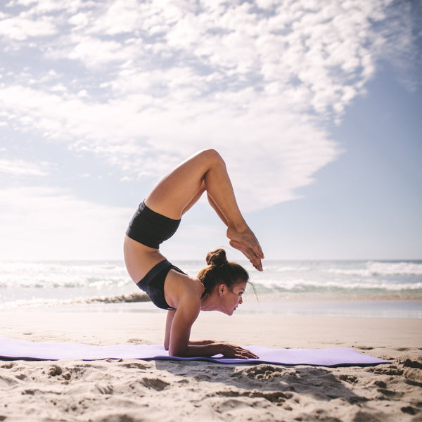 Woman practicing yoga on a beach with ocean and sky in the background